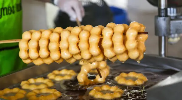 Des beignets dorés, en forme de chaînette, sont frits dans l'huile. La pâte à beignets prend forme, prête à être dégustée.
