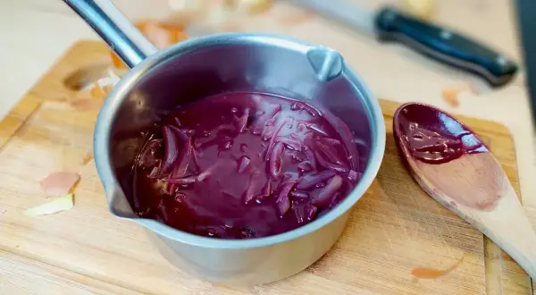 Sauce porto facile mijotant dans une casserole, avec des oignons rouges et une cuillère en bois.
