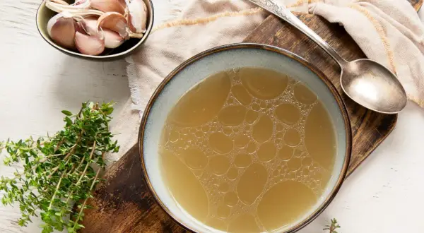 Un bol de bouillon de volaille doré, avec de l'ail et du thym. Idéal pour savoir comment faire un bouillon de volaille savoureux.