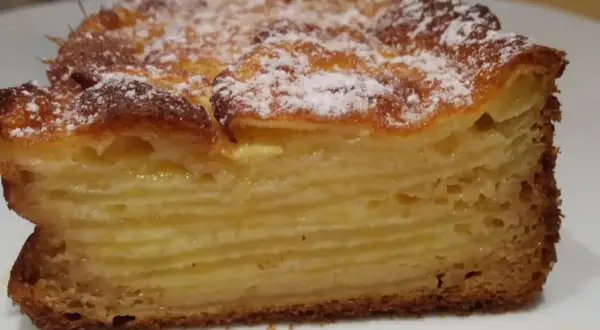 Tranche d'un gâteau aux pommes, feuilleté et doré, saupoudré de sucre glace. Un délice invisible aux pommes.