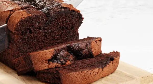 Un délicieux gâteau au chocolat sans beurre, coupé en tranches sur une planche en bois. Sa texture moelleuse et son goût intense invitent à la gourmandise.