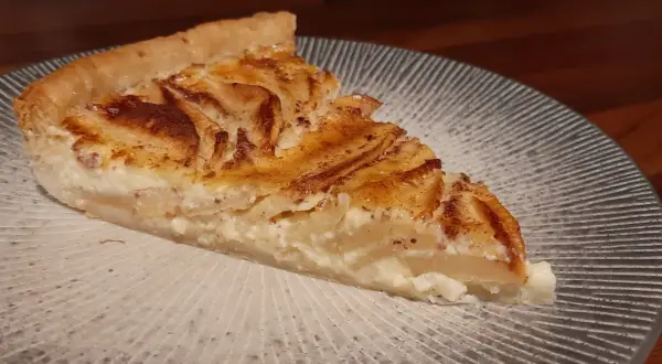 Une part de tarte aux pommes à l'ancienne, avec sa garniture crémeuse et ses pommes caramélisées, sur une assiette décorée.