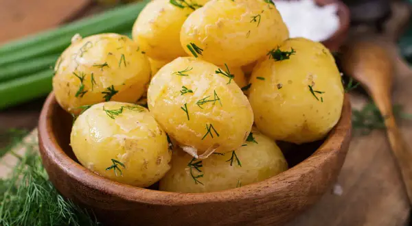 Pommes de terre à l'eau, tendres et parsemées d'aneth frais, dans un bol en bois. Un plat simple et savoureux.