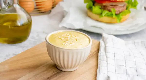 Sauce burger maison crémeuse, garnie de flocons, prête à accompagner un burger savoureux. Huile d'olive et œufs en arrière-plan.