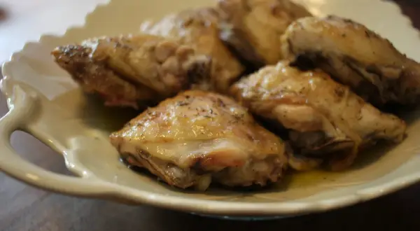 Plusieurs hauts de cuisse de poulet au four, dorés et assaisonnés d'herbes, reposent sur une assiette blanche festonnée.