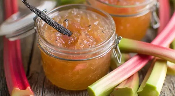 Confiture de rhubarbe maison dans un bocal, avec des tiges de rhubarbe fraîches et une gousse de vanille.