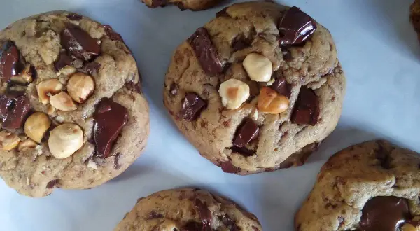 Gros plan sur des cookies américains faits maison, débordant de pépites de chocolat noir et de noisettes. Parfaits pour une recette de cookies américain gourmande.