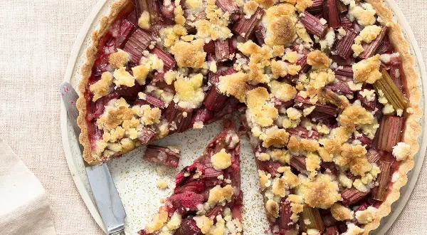 Tarte crumble à la rhubarbe, une délicieuse recette avec rhubarbe, garnie de morceaux de fruits rouges et d'une pâte croustillante.