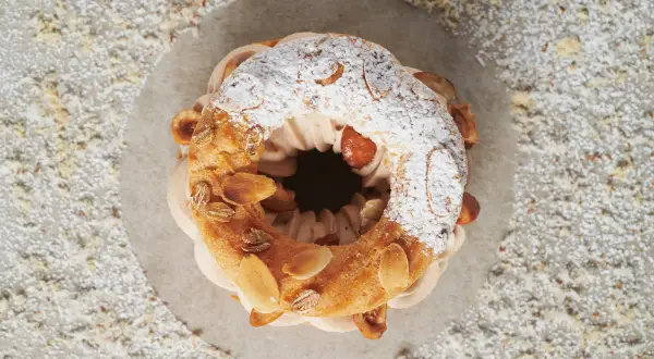 Un délicieux Paris-Brest, saupoudré de sucre glace et garni d'amandes grillées, attend d'être dégusté.
