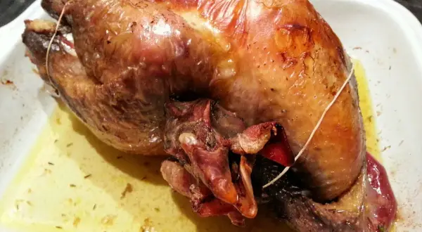 Une pintade au four, dorée et juteuse, repose dans un plat blanc, baignant dans son jus savoureux.