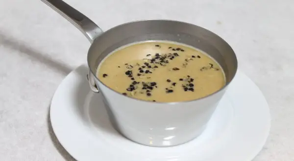 Sauce au poivre recette de chef, onctueuse et garnie de grains de poivre concassés, servie dans une petite casserole en métal sur une assiette blanche.