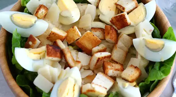 Salade César appétissante dans un bol en bois, garnie d'œufs durs, de croûtons dorés et d'une onctueuse sauce César.