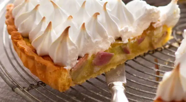 Une part de tarte rhubarbe meringuée, avec sa croûte dorée et sa garniture acidulée, surmontée d'une meringue légère et aérienne.