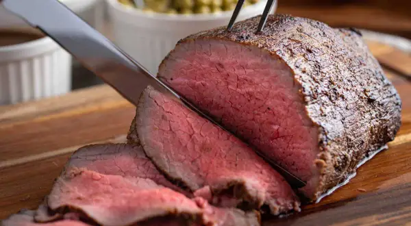 Un délicieux rôti de boeuf, coupé en fines tranches rosées, est prêt à être servi avec des accompagnements.