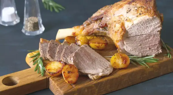 Un gigot de 7 heures, tendre et savoureux, servi avec des pommes de terre rôties et du romarin sur une planche en bois.