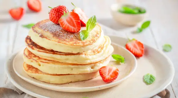 Pile de pancakes moelleux, parsemés de sucre glace et ornés de fraises fraîches et de menthe. Un délice digne des pancakes Cyril Lignac.