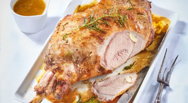 Gigot d'agneau rôti, doré et juteux, garni de romarin frais. Un délice pour la cuisson parfaite.