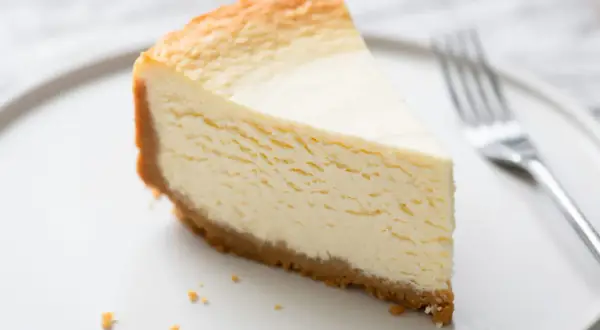 Une part de gâteau au fromage blanc onctueux, digne d'un gâteau au fromage blanc Cyril Lignac, sur une assiette blanche avec une fourchette.