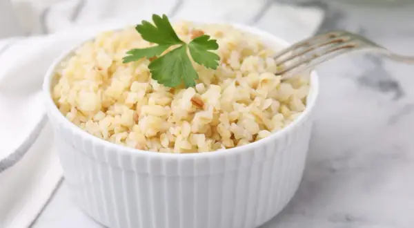 Un bol de boulgour cuit, garni d'une feuille de persil, prêt à être dégusté. La cuisson du boulgour est simple et rapide.