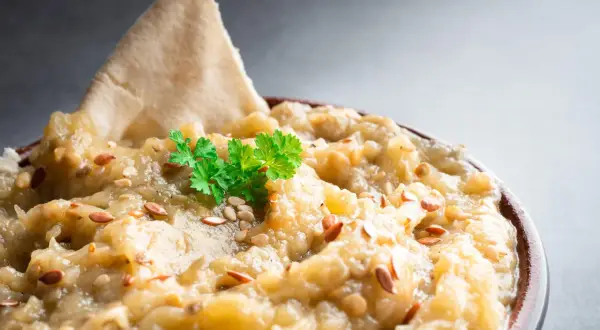 Un bol de le vrai caviar d'aubergine, garni de persil frais et de graines de sésame, avec un morceau de pain pita.