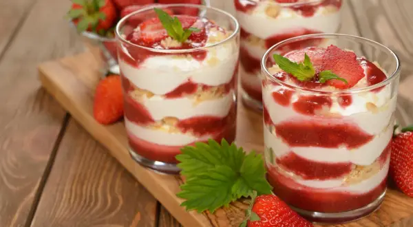 Délicieux tiramisu fraise en verrines, alternant couches de crème, biscuits émiettés et coulis de fraises, garni de fruits frais et de menthe.