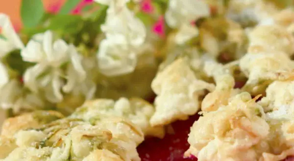 Délicieux beignets de fleur d'acacia à la poêle, saupoudrés de sucre, avec des fleurs fraîches en arrière-plan.
