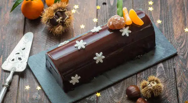 Bûche marron glacé, décorée de flocons et de quartiers de clémentine, évoquant la magie de Noël.