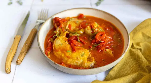 Un plat de poulet basquaise, préparé au Cookeo, servi dans un bol avec des poivrons rouges et verts, garni de thym.