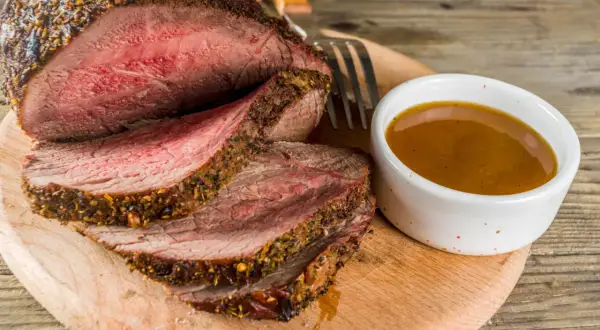 Un délicieux roti de boeuf basse température, tranché et servi avec une sauce savoureuse sur une planche en bois.