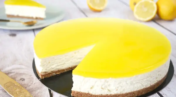 Cheesecake citron mascarpone, un délice jaune vif sur fond de bois. Une part est déjà servie.