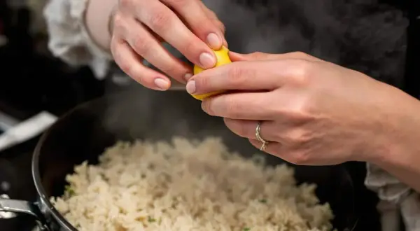Cuisson du riz rouge : une main presse un quartier de citron sur le riz fumant dans une casserole.