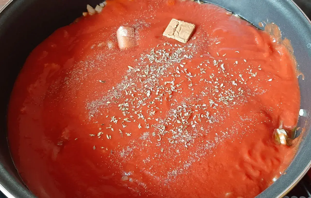 Sauce tomate maison mijote dans une poêle, agrémentée d'herbes et d'un cube de bouillon.