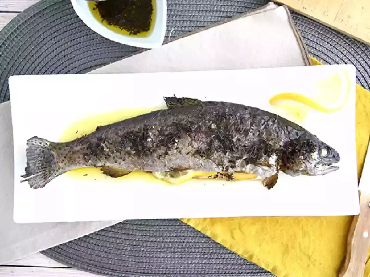 Une truite au four entière, dorée et savoureuse, servie sur une assiette blanche avec des quartiers de citron. Un délice simple et sain.