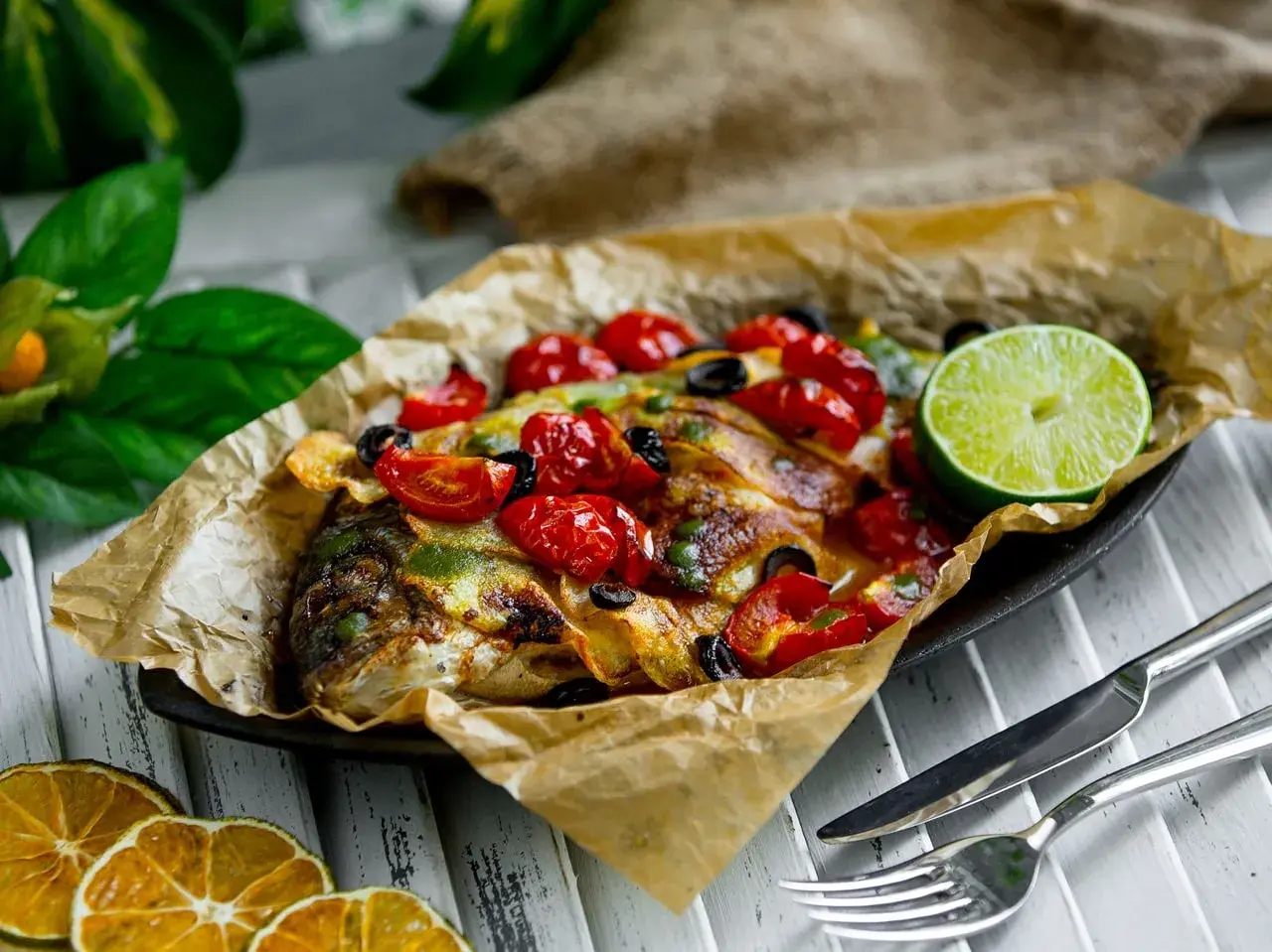 Dorade en papillote, savoureuse et colorée, garnie de tomates cerises, d'olives et d'une tranche de citron vert.