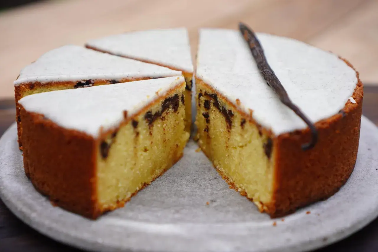 Gâteau poudre d'amande facile et rapide, avec glaçage blanc et éclats de chocolat. Une gousse de vanille décore ce délice.