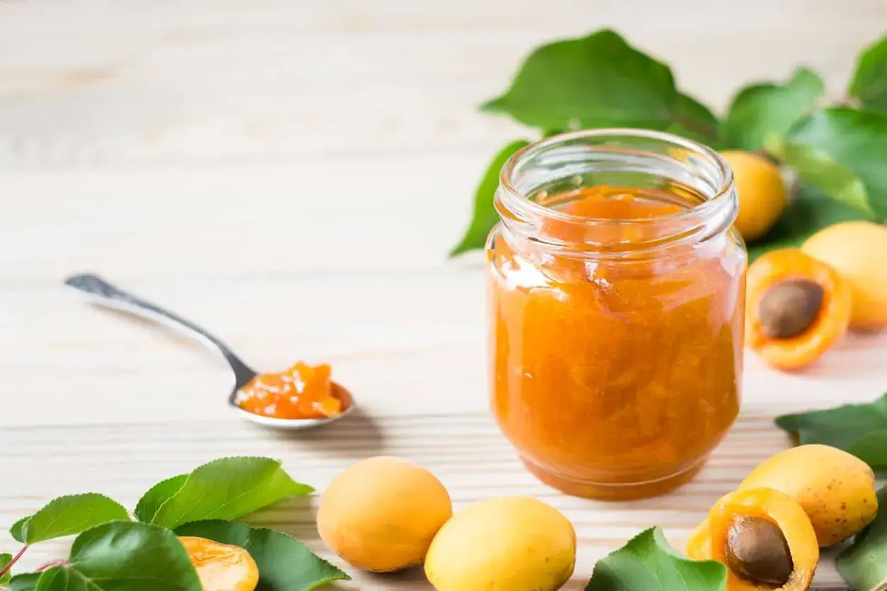 Un pot de confiture abricot peu sucrée, avec des abricots frais et une cuillère remplie de cette délicieuse confiture.
