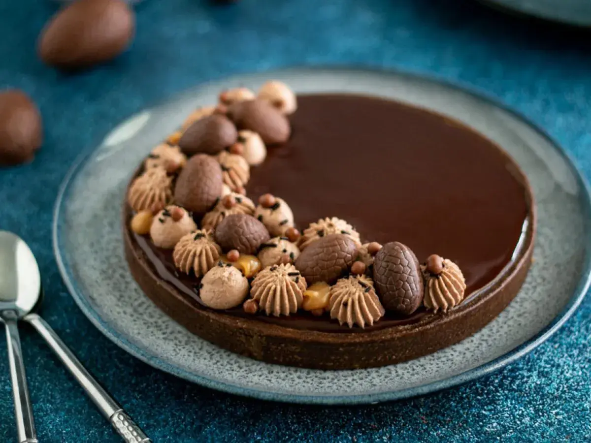 Délicieuse tarte chocolat caramel, ornée d'œufs en chocolat et de touches de crème, prête à être dégustée.