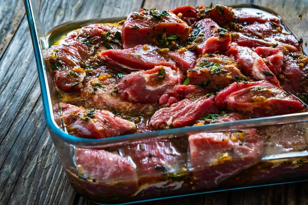 Morceaux de joue de porc marinés dans un plat en verre, prêts pour une délicieuse recette.