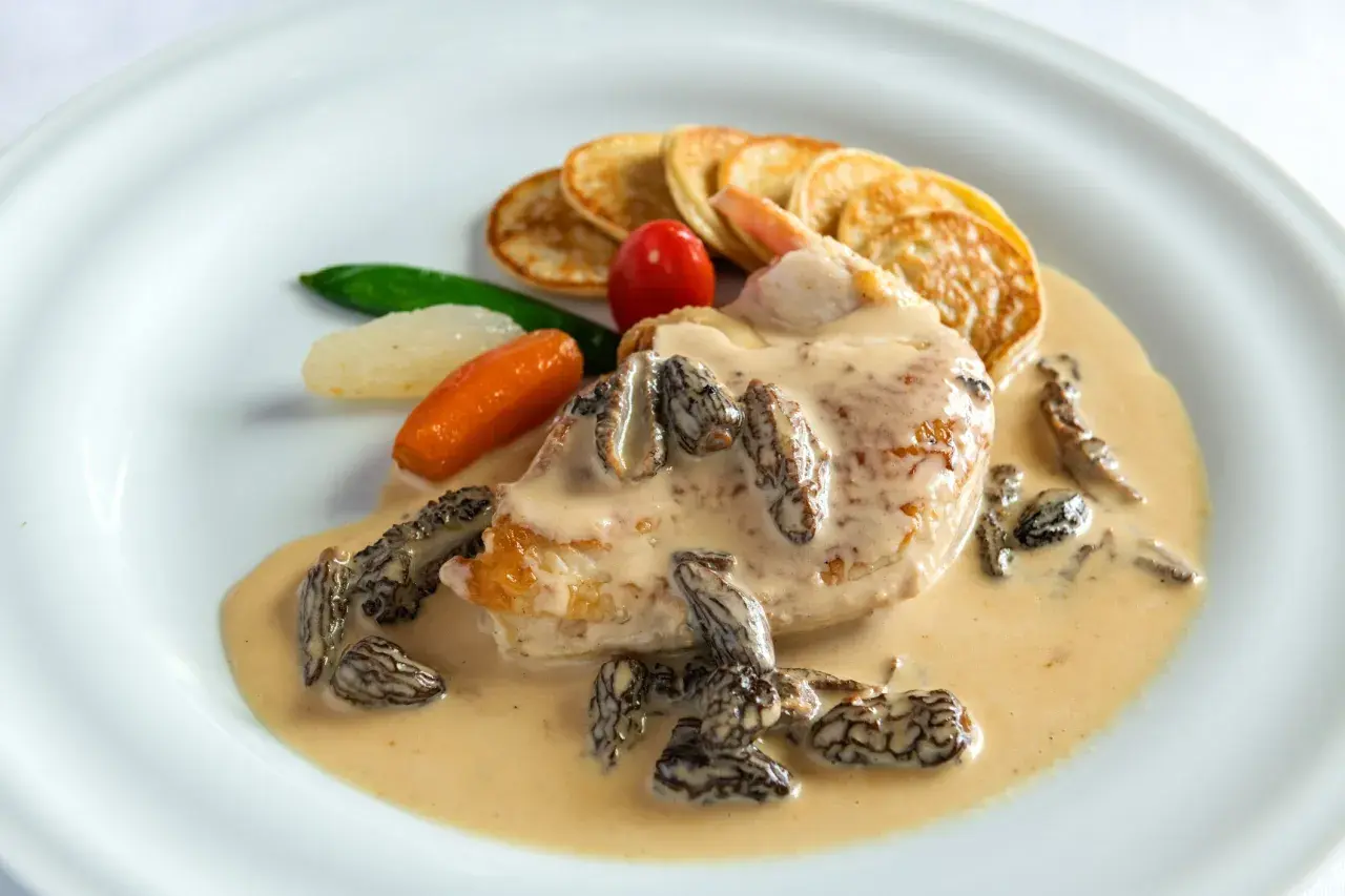 Un plat de poulet en sauce crémeuse avec des morilles, des mini-crêpes, des carottes et des petits pois. Le jus de poulet est riche et onctueux.