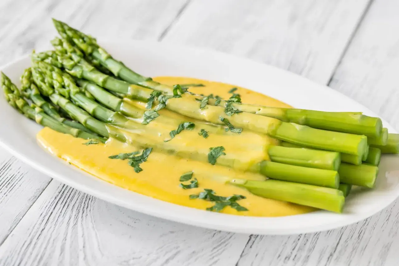 Asperges vertes fraîches nappées d'une sauce onctueuse et dorée, parsemées d'herbes. Un délice de sauce pour asperges chaudes.