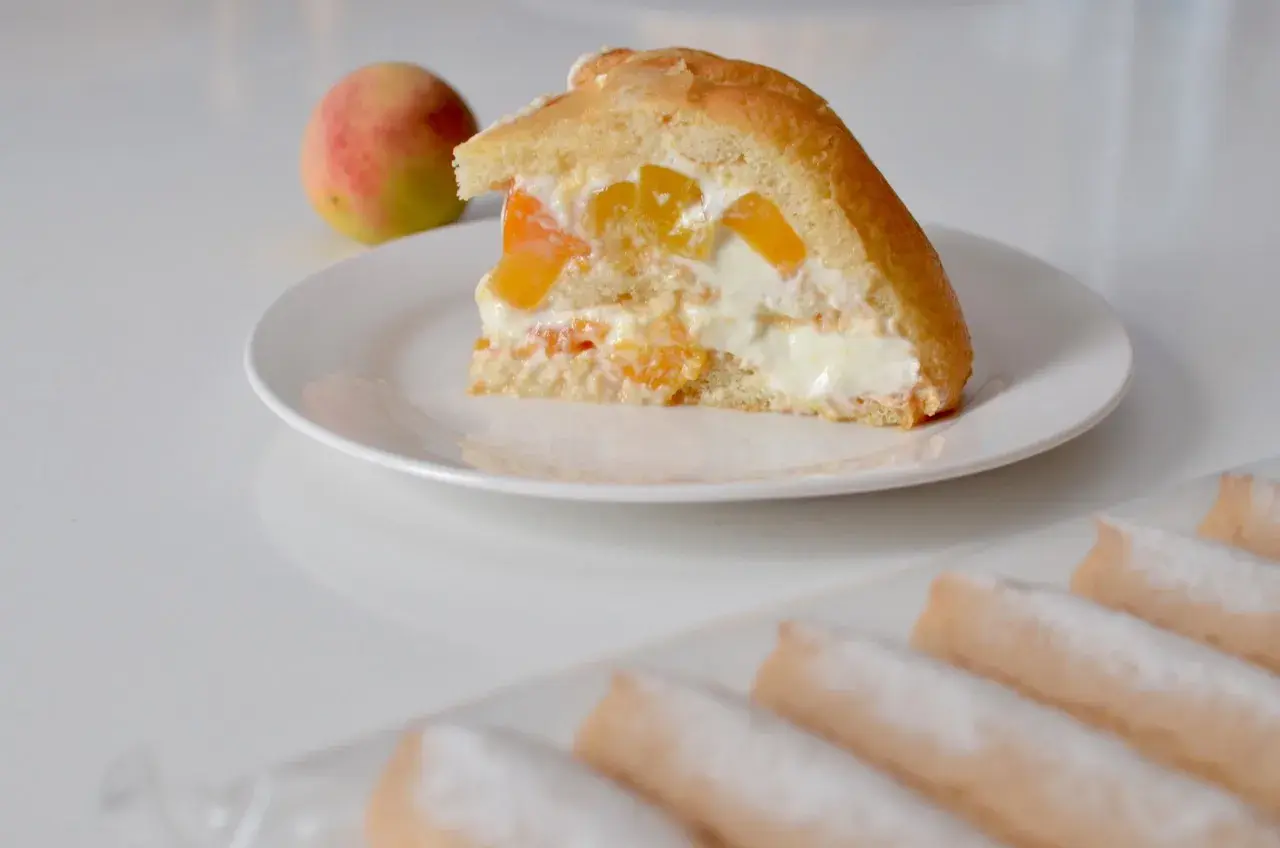 Tranche de charlotte aux fruits et fromage blanc, garnie de morceaux de pêche et de crème onctueuse. Un délice fruité et léger.
