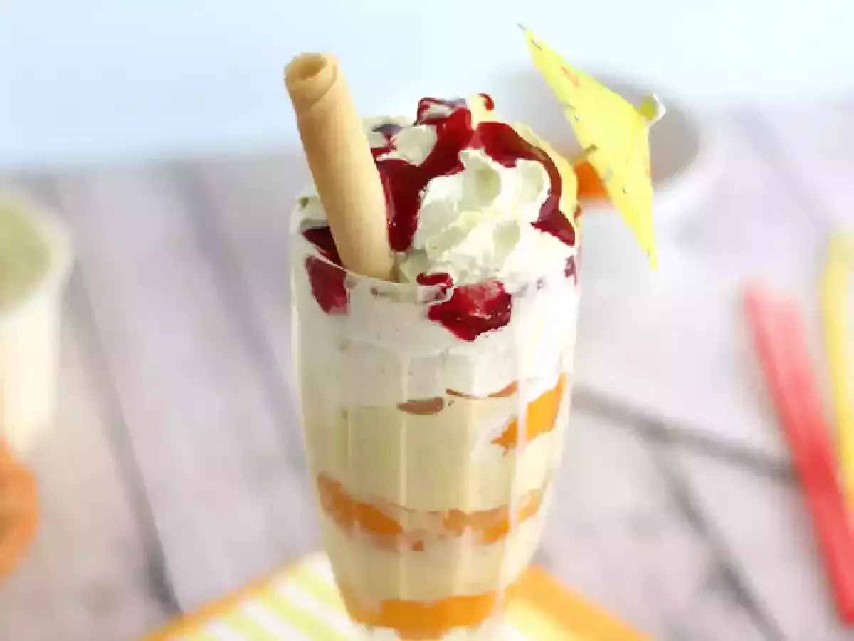 Un déliceux pêche Melba, avec des couches de fruits, de crème fouettée et de coulis de fruits rouges, garni d'une gaufrette et d'un petit parasol.