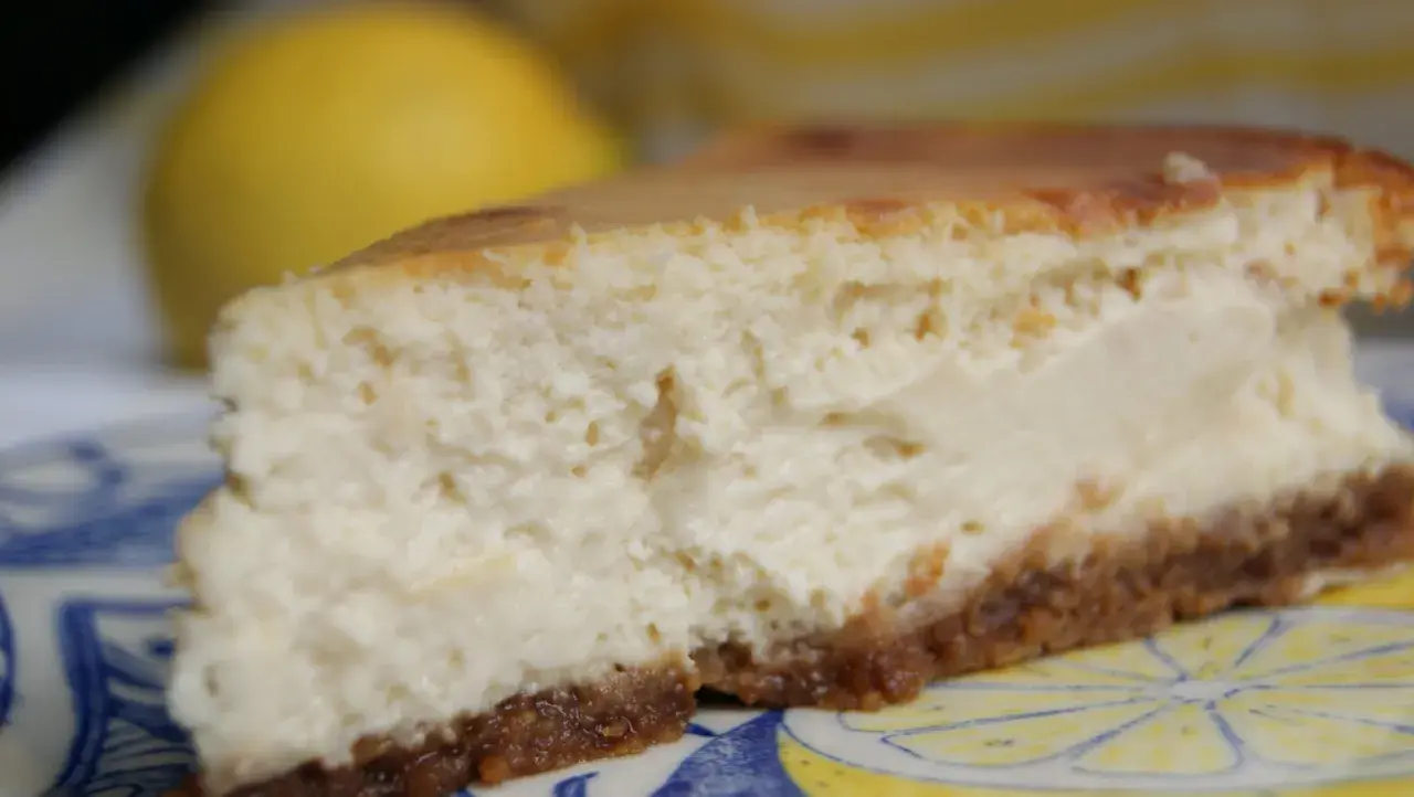 Tranche de cheesecake ricotta citron, crémeuse et légère, sur une assiette décorée de citrons.