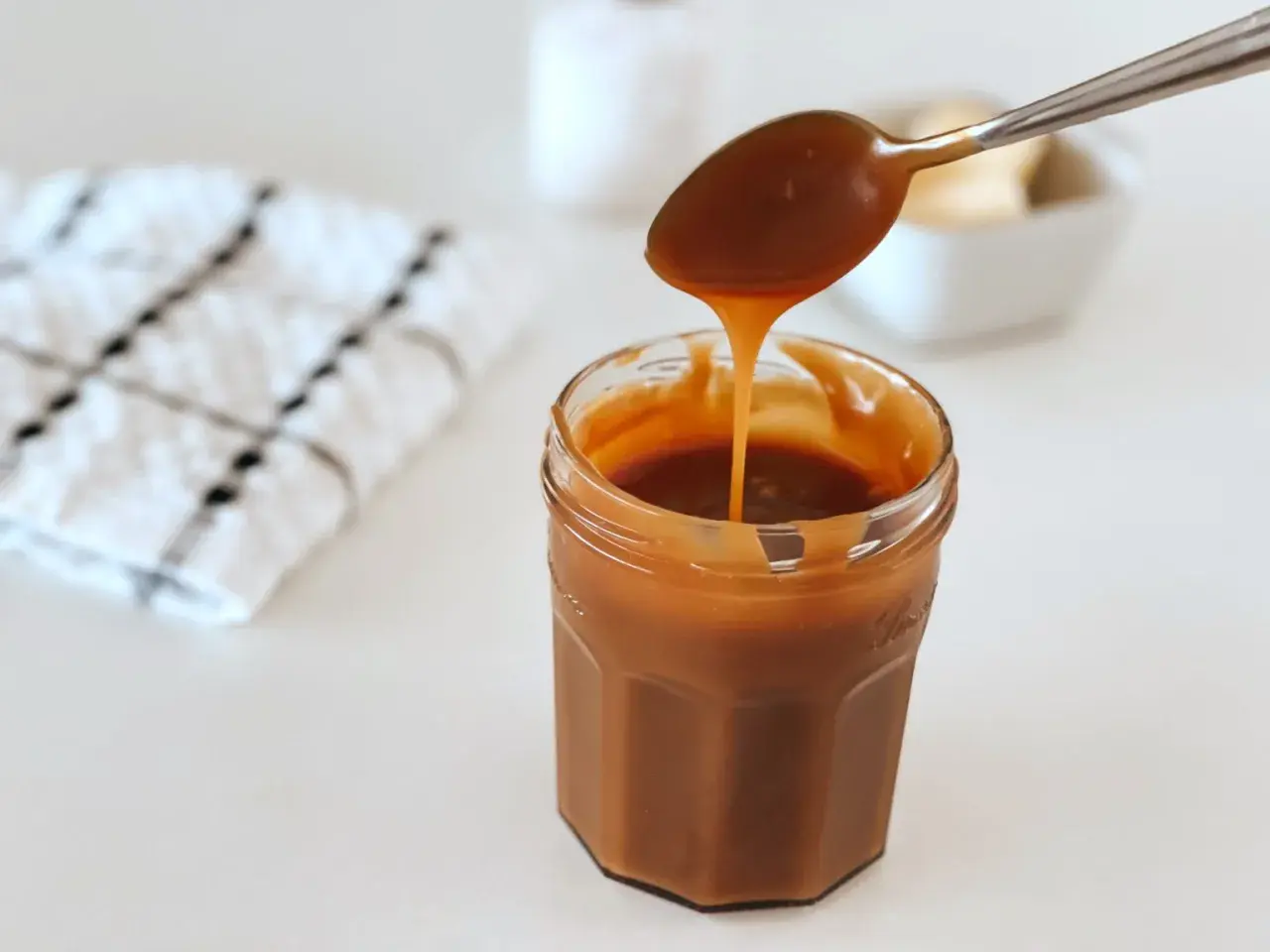 Une cuillère verse un caramel beurre salé onctueux dans un pot en verre.