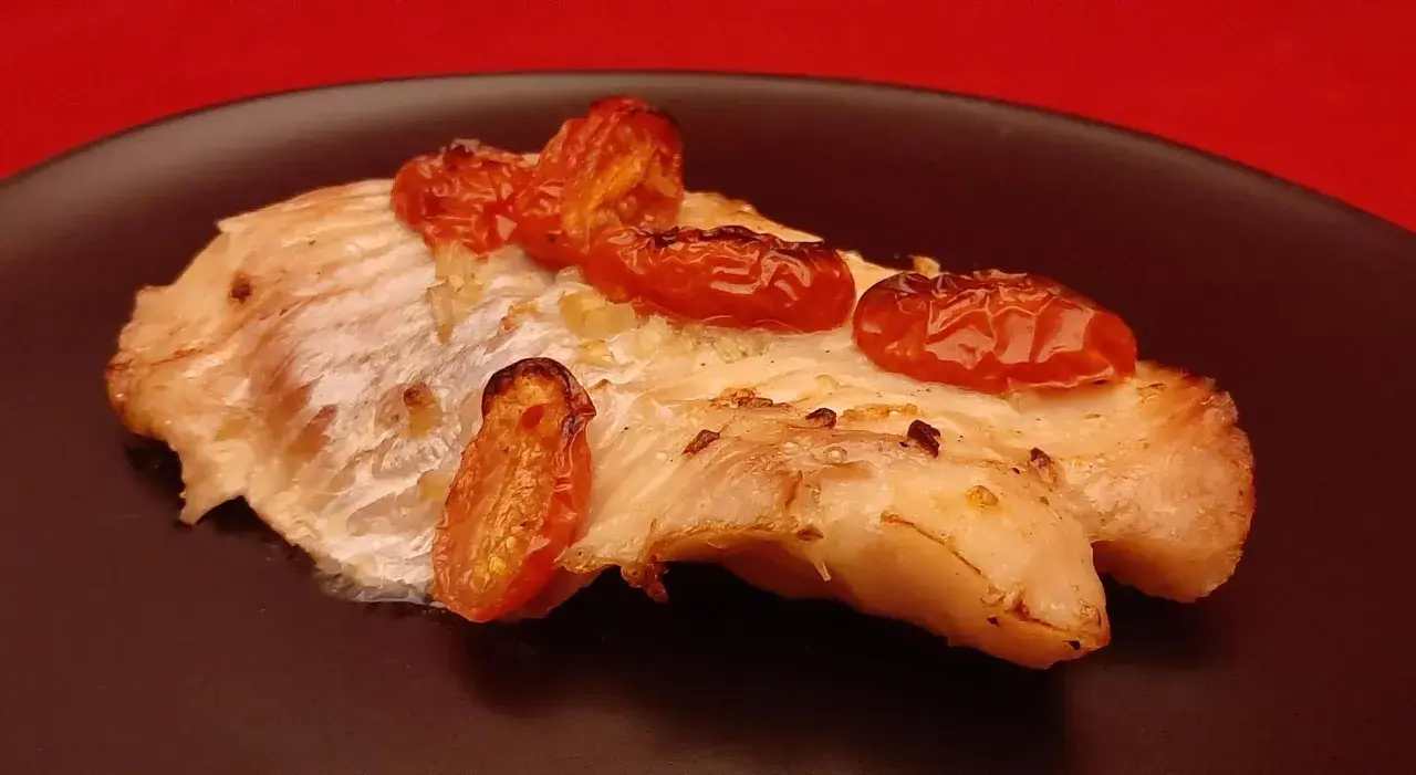 Un délicieux filet de dorade au four, garni de tomates cerises rôties, sur une assiette noire.