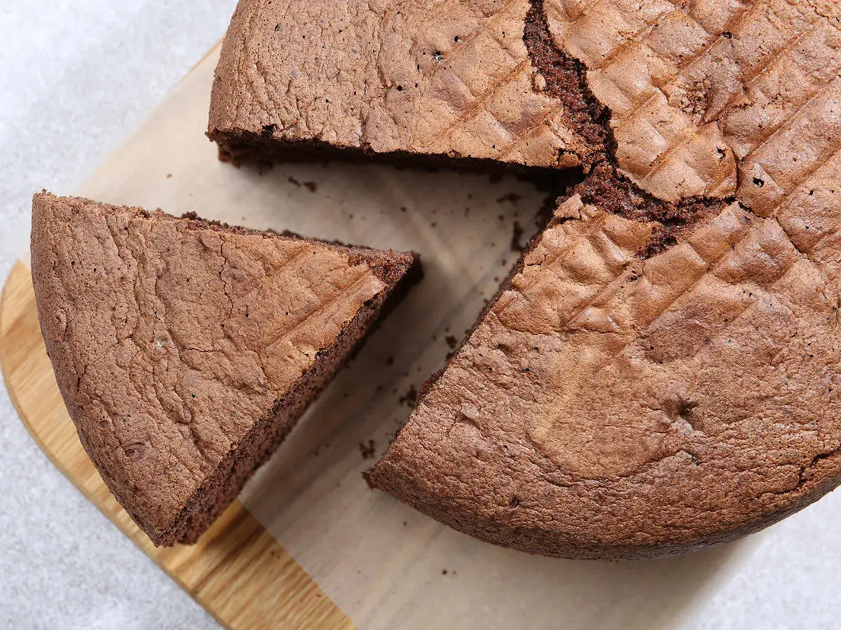 Un gâteau chocolat Pierre Hermé, moelleux et aérien, avec une part coupée sur une planche en bois.