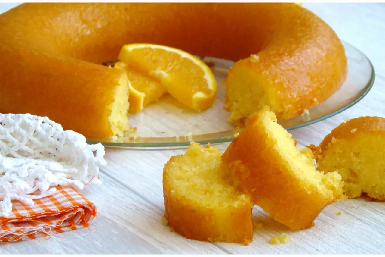 Un délicieux cake à l'orange, avec des tranches d'orange fraîche, servi sur une assiette en verre. Une part est déjà coupée.