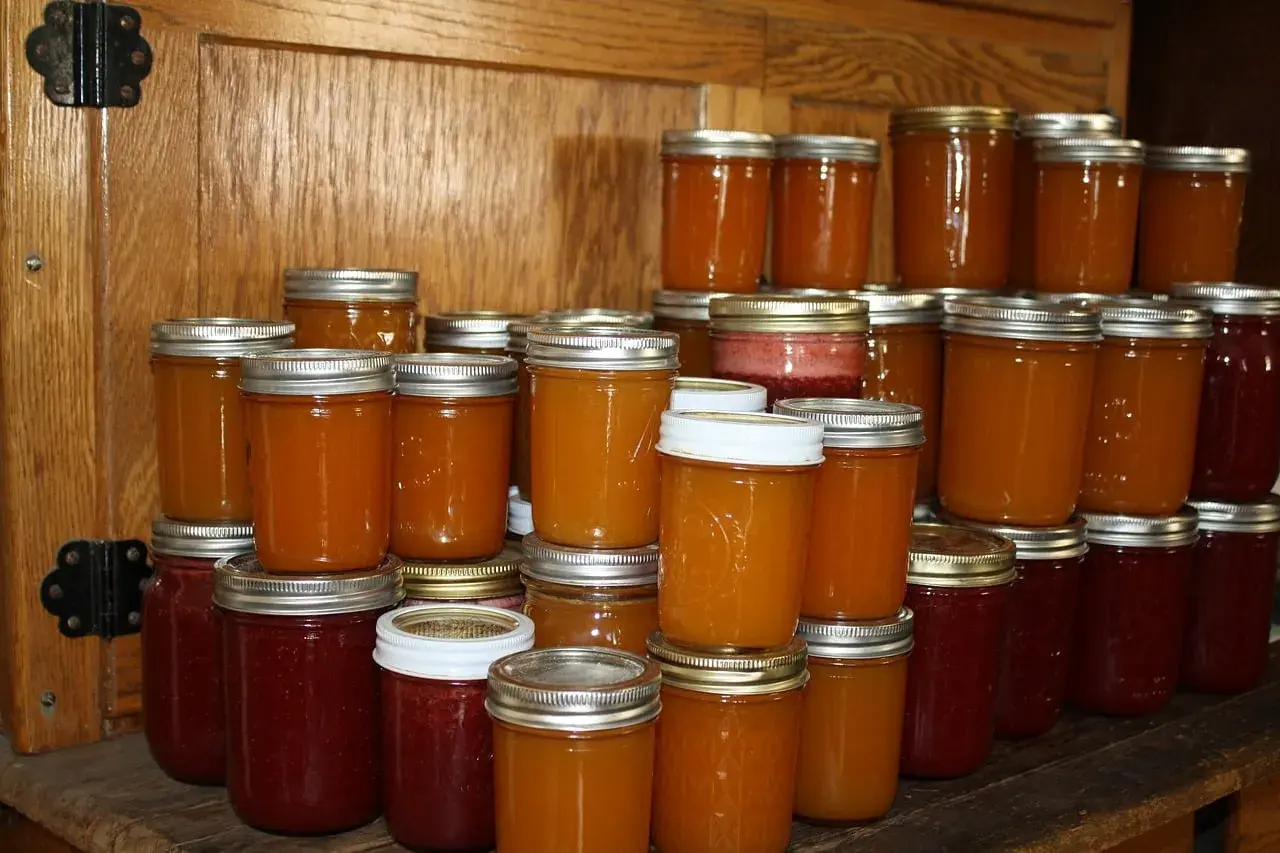 Des bocaux de confiture de coing, certains d'un rouge profond, d'autres d'un orange doré, empilés sur des étagères en bois.