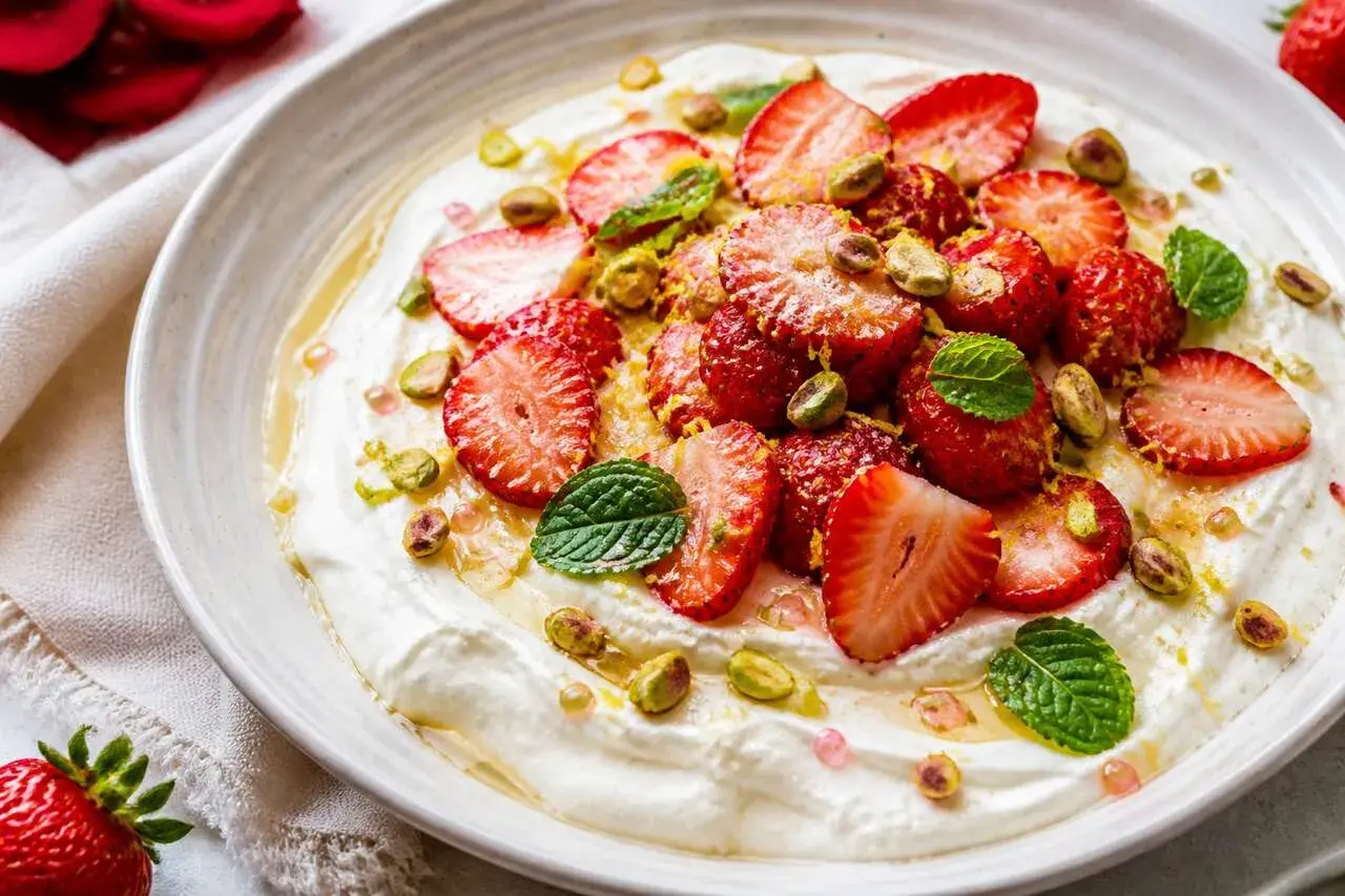 Délicieuse salade de fruits maison : fraises fraîches, pistaches croquantes et menthe fraîche sur une crème onctueuse, arrosée de miel.