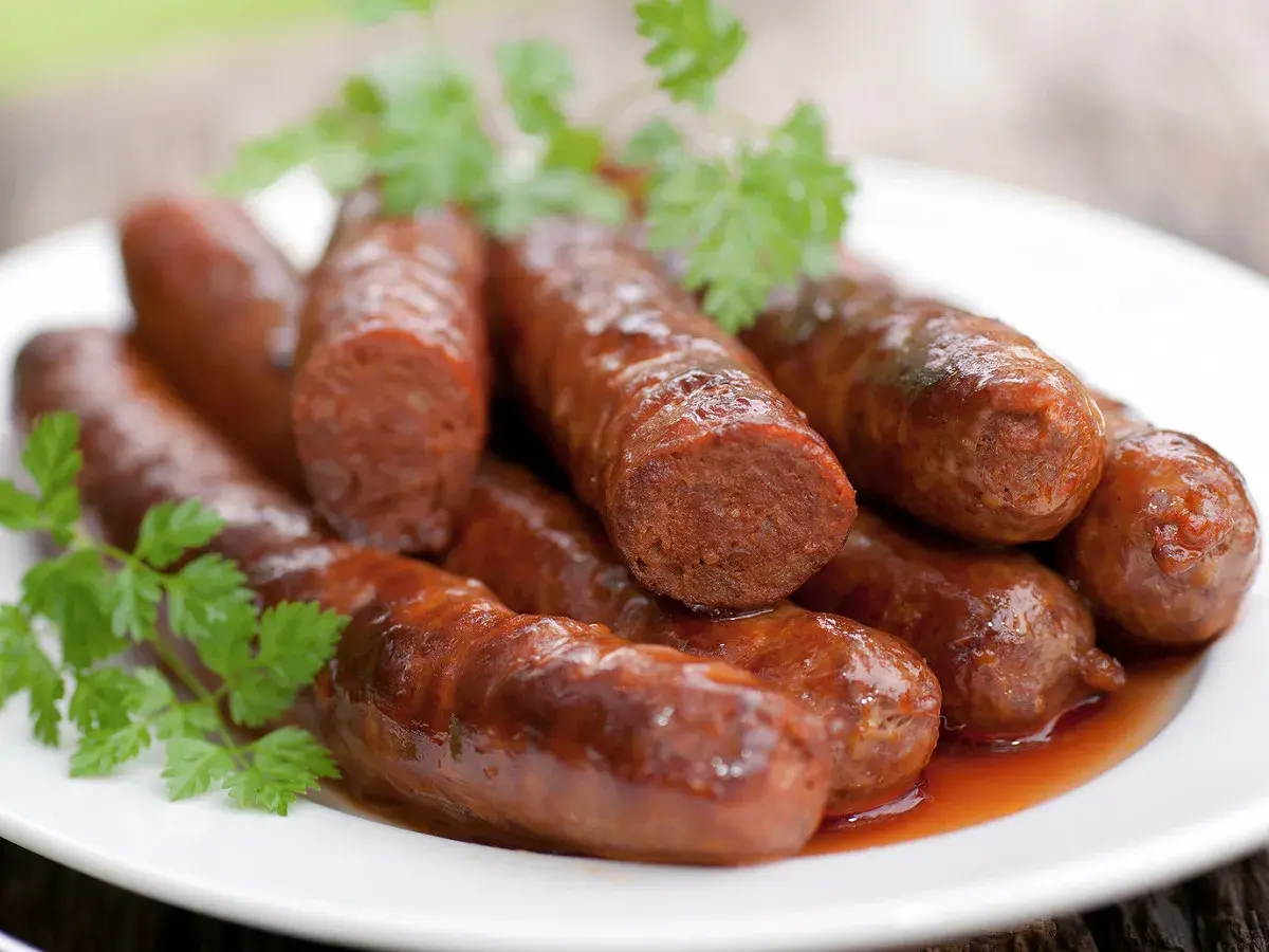 Assiette de merguez au four, dorées et juteuses, garnie de persil frais. Un délice prêt à être dégusté.